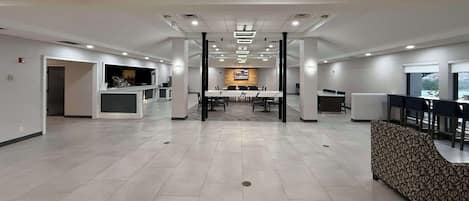 Een ruime, moderne hotellobby met een lange receptiebalie, een centrale vergadertafel en een gestreept bankje.