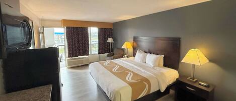 Une chambre d’hôtel avec un grand lit, deux lampes de chevet, une télévision et une vue sur l’extérieur.
