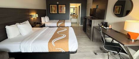 Habitación de hotel con dos camas, un escritorio, una silla, un espejo y una kitchenette.