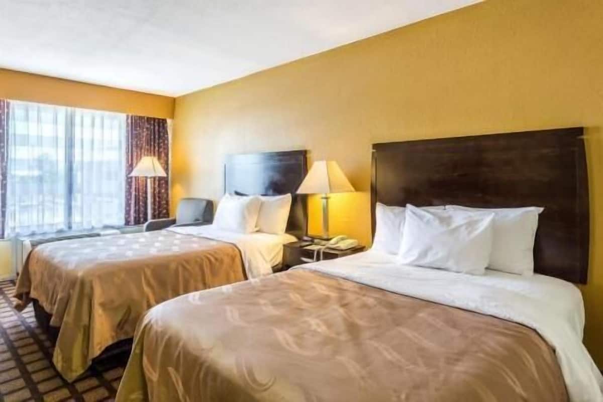 A hotel room with two beds, a large window with curtains, and a flat-screen TV on the wall.