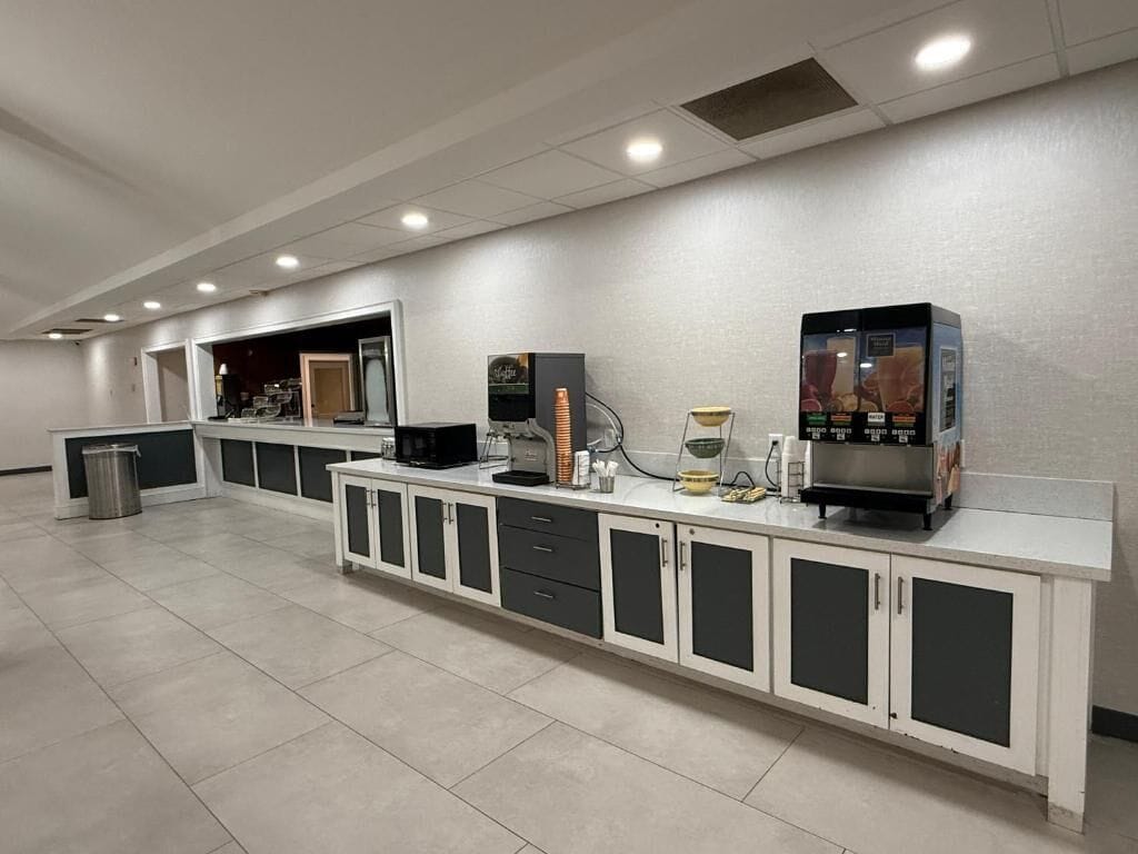 A long counter with a coffee machine and a small refrigerator. There are cabinets and drawers along the counter.
