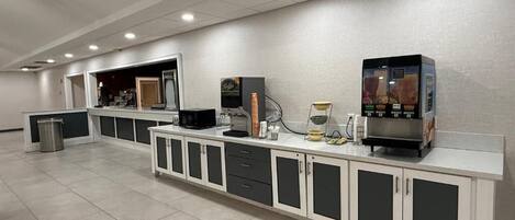 A long counter with a coffee machine and a small refrigerator. There are cabinets and drawers along the counter.