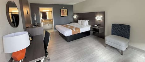 A hotel room with a bed, desk, chair, and a mirror.
