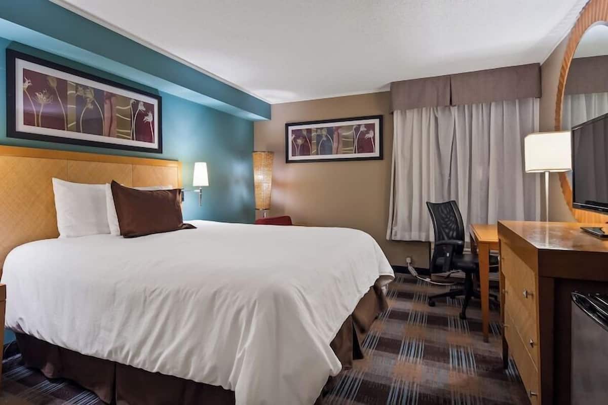 A hotel room with a bed, desk, TV, and two wall-mounted lamps.