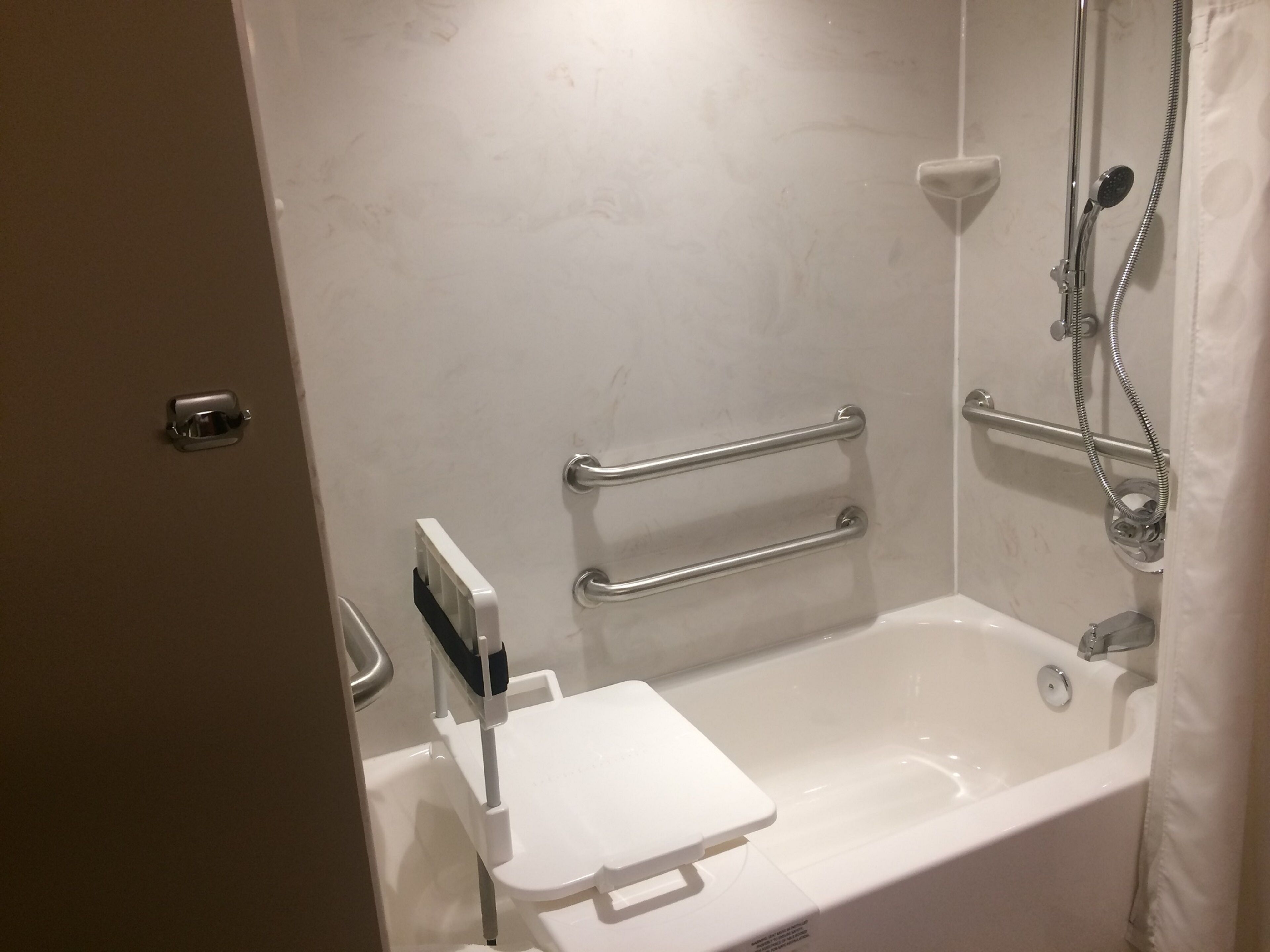 Ein Badezimmer mit einer weißen Badewanne, Haltegriffen, einer Handbrause und einer weißen Toilette.