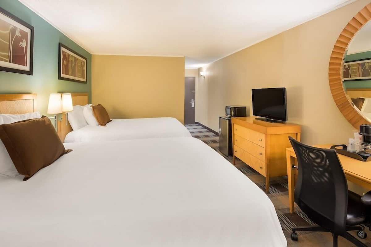 A hotel room with two beds, a desk, a television, and a mirror.