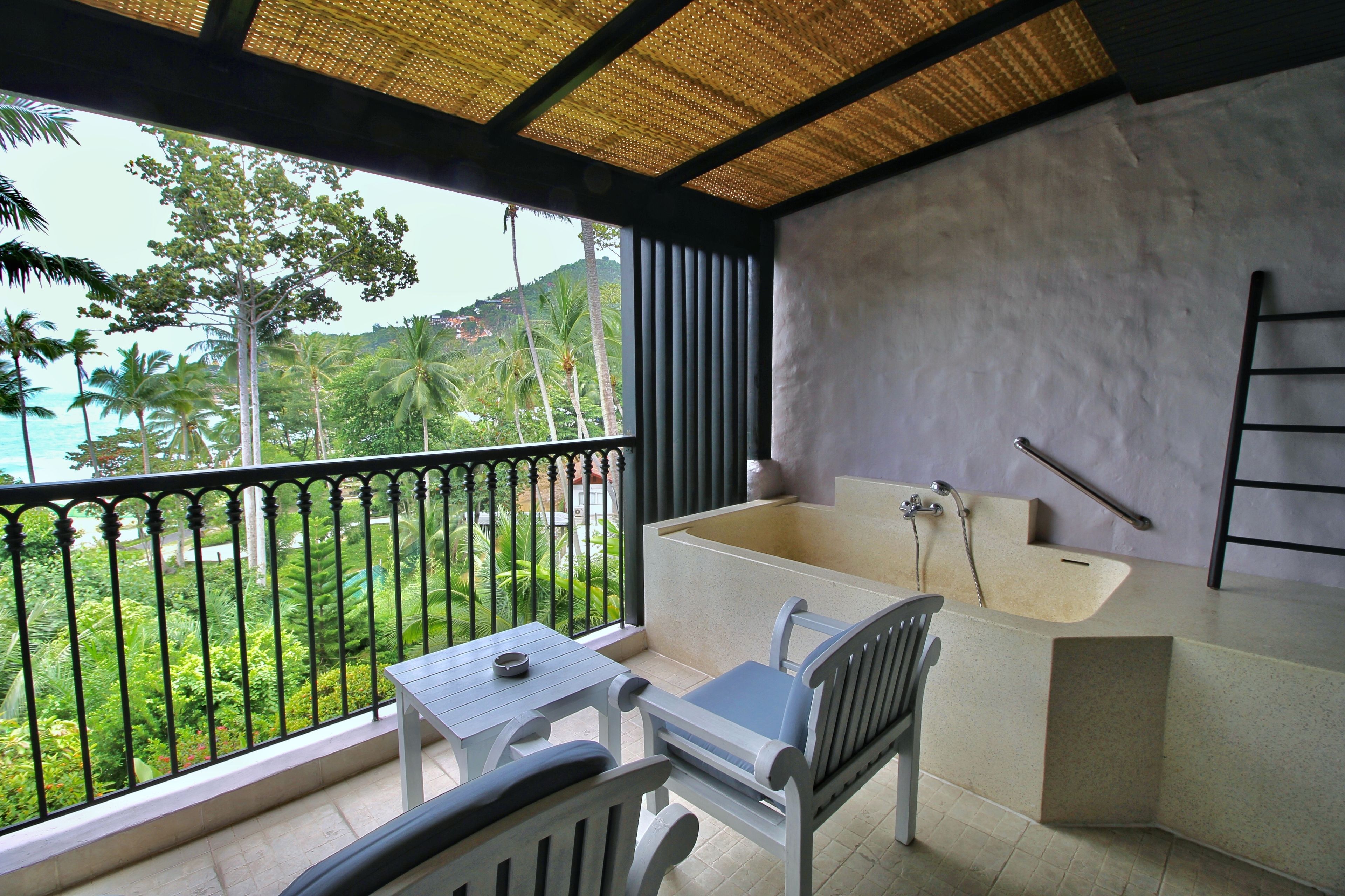 Un balcon avec vue sur les palmiers et la plage, une petite table, une chaise et une baignoire.