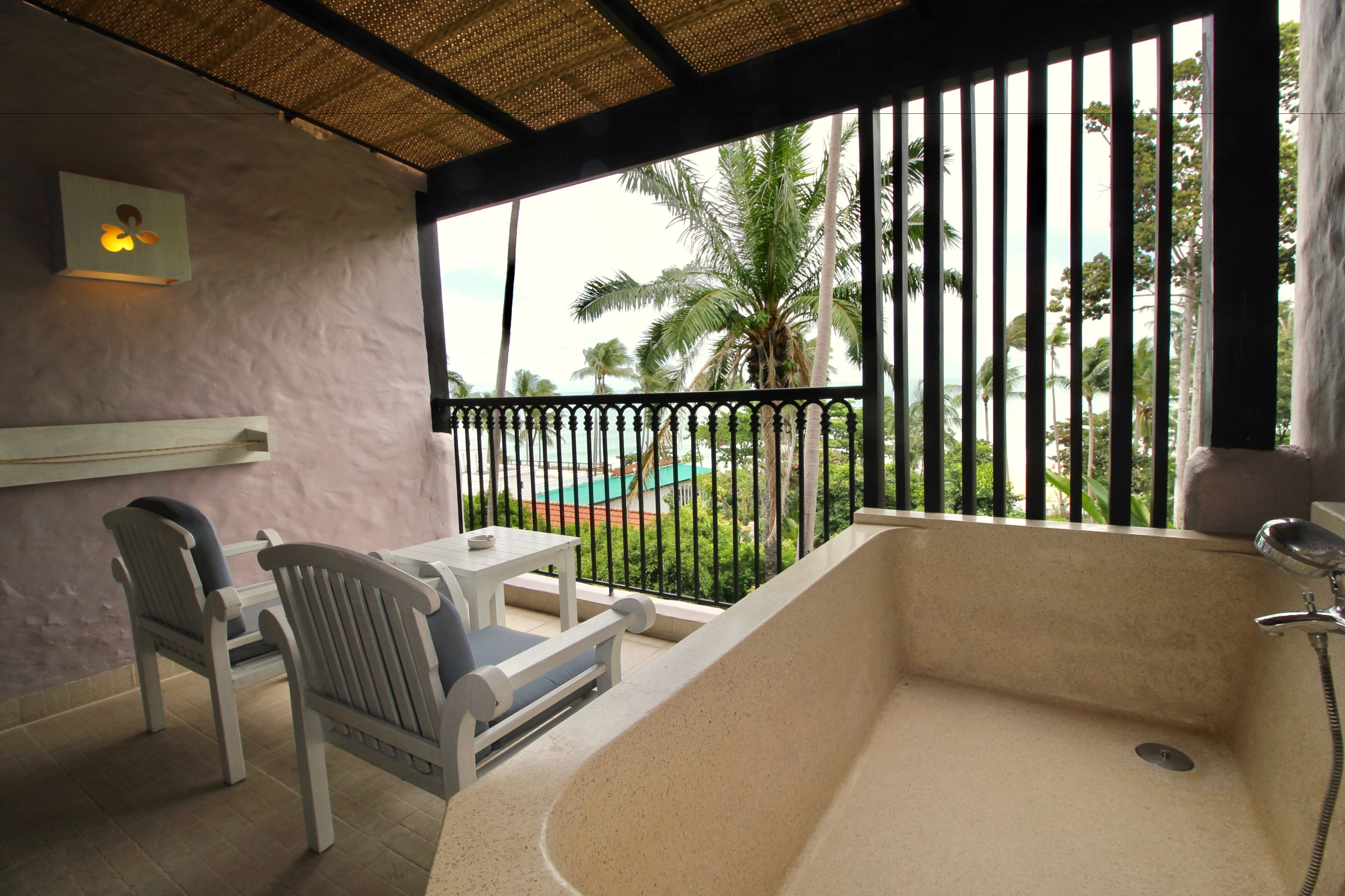 Un balcon avec une baignoire, des chaises et une table.
