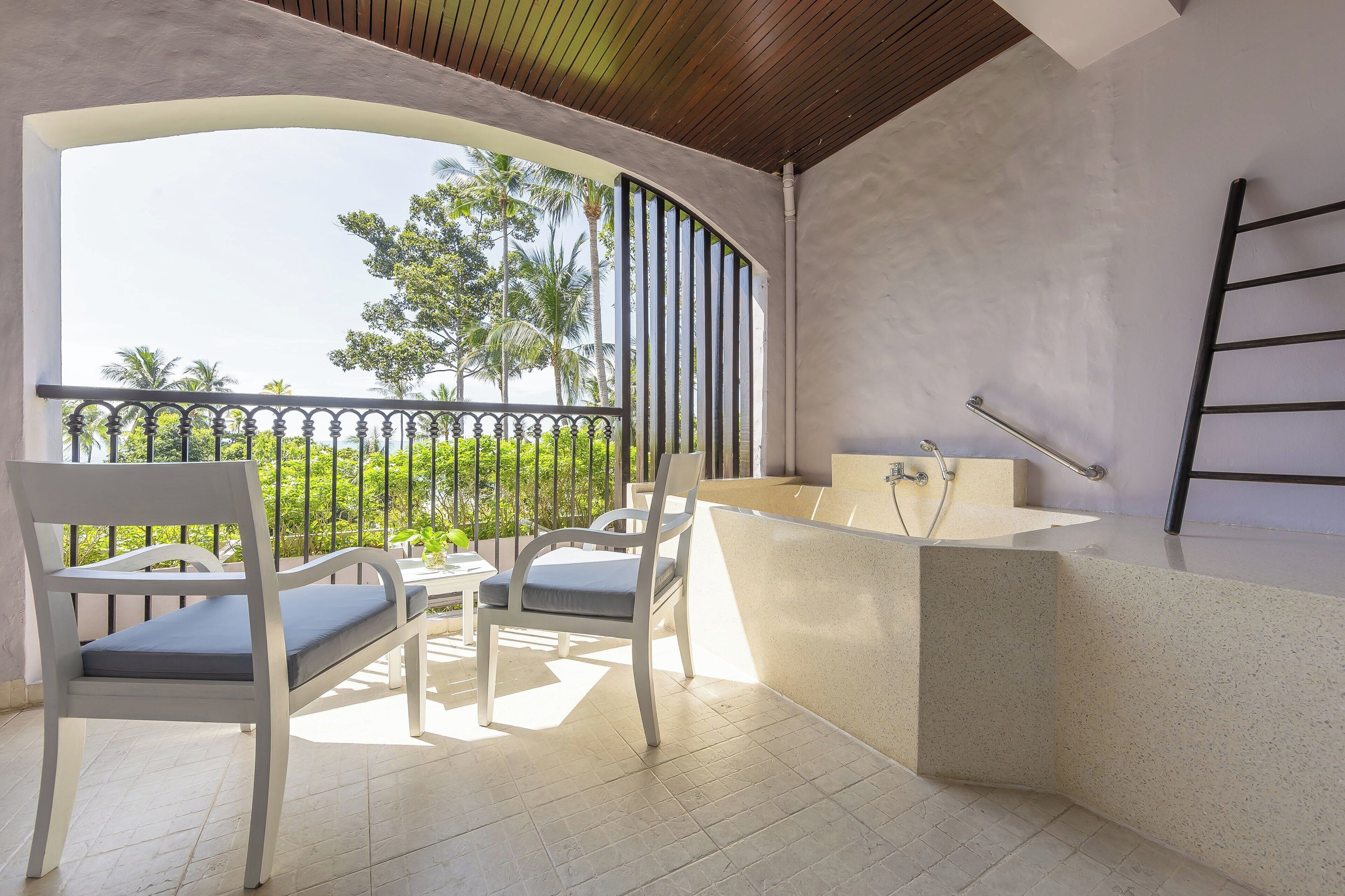 A balcony with two white chairs, a small table, and a bathtub.