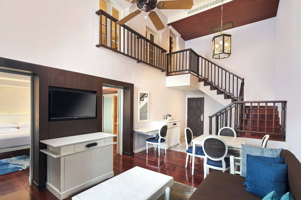 A spacious living area with a flat-screen TV, a dining table with chairs, a sofa, and a staircase leading to an upper level.