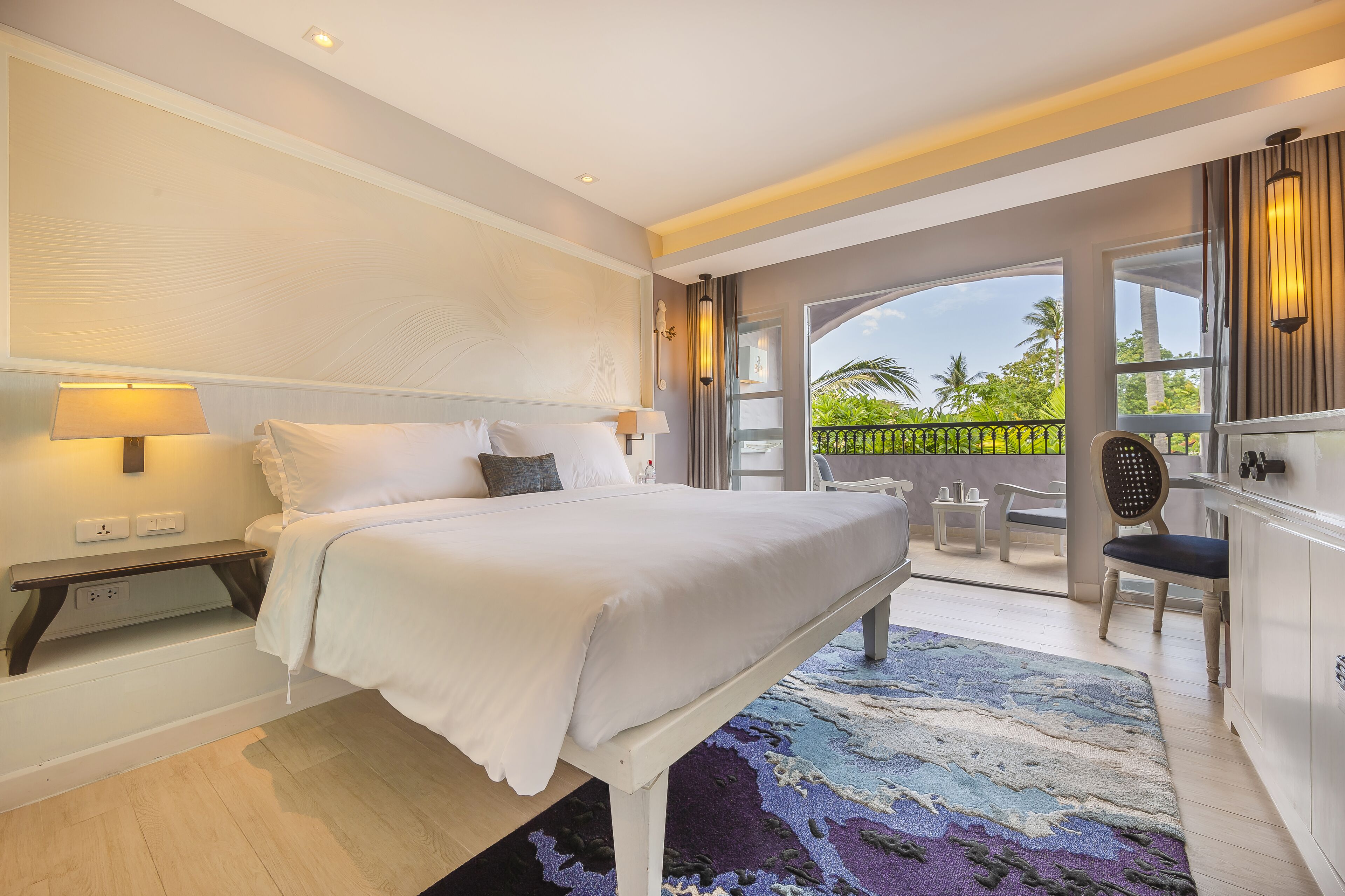 Una habitación de hotel moderna con una cama grande, mesitas de noche, un escritorio y vistas al exterior.