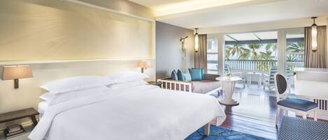 Habitación de hotel con una cama grande, un área de estar con sofá y sillones, un balcón con vistas, y un escritorio con silla.