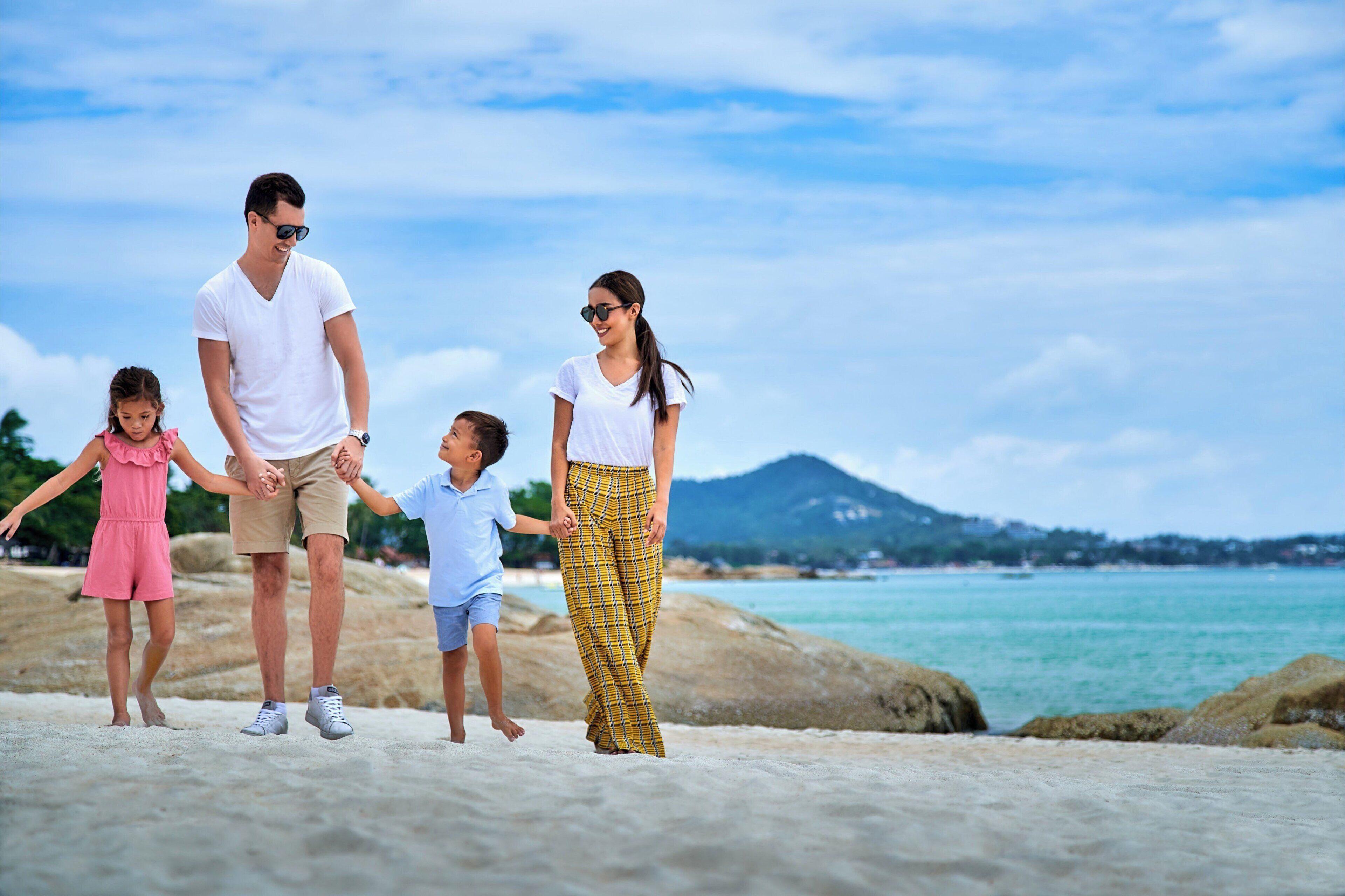 A family walking on a sandy beach with a clear sky and a mountain in the background.