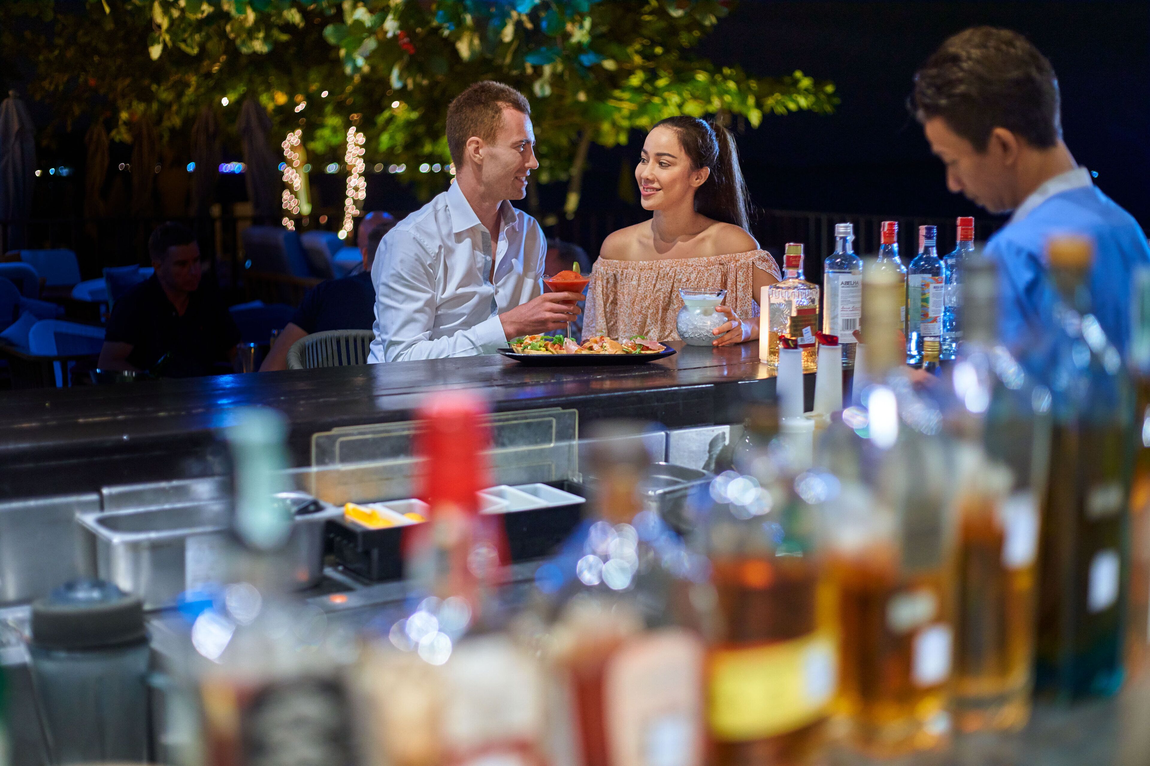 Un espace bar avec un comptoir, diverses bouteilles et une personne tenant un verre.