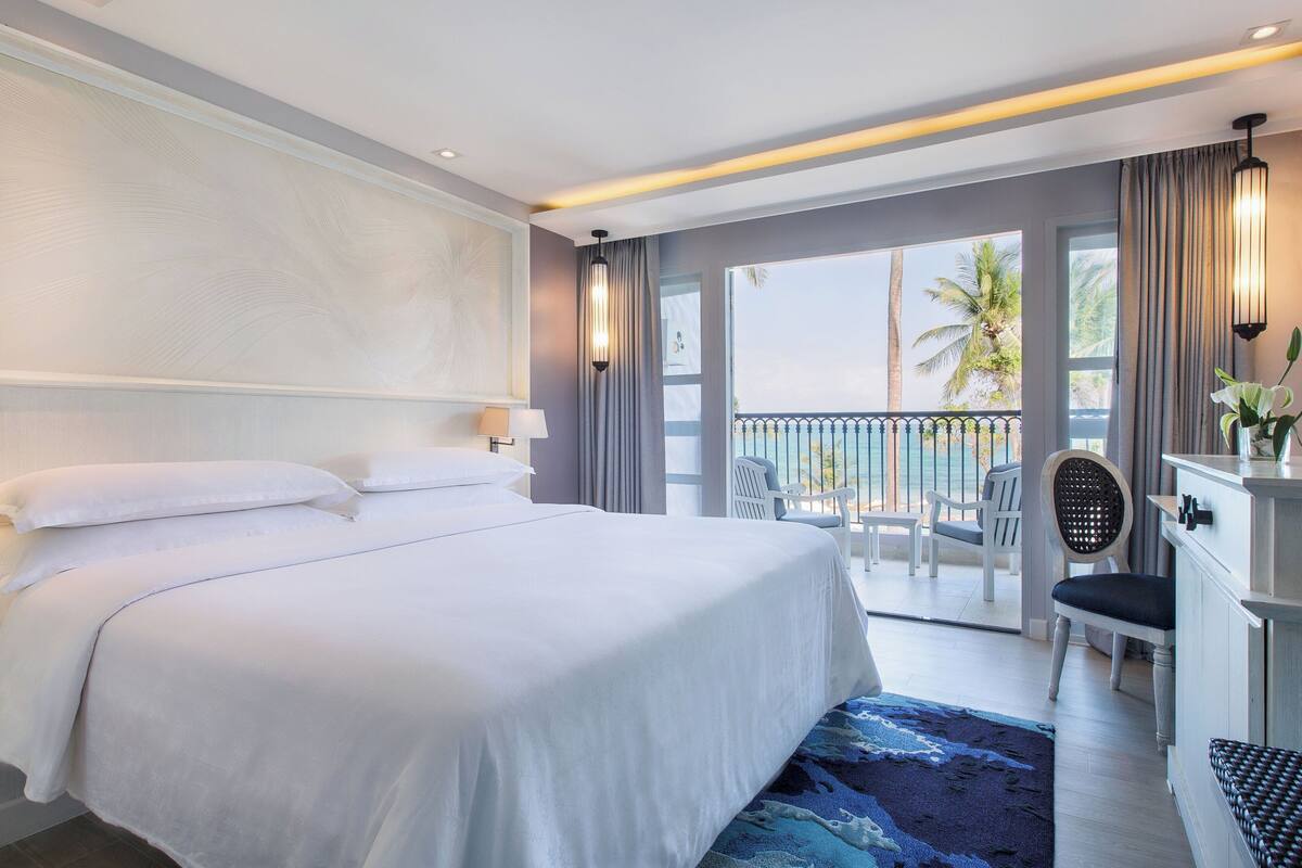 A hotel room with a large bed, a balcony with a view, and a desk with a chair.