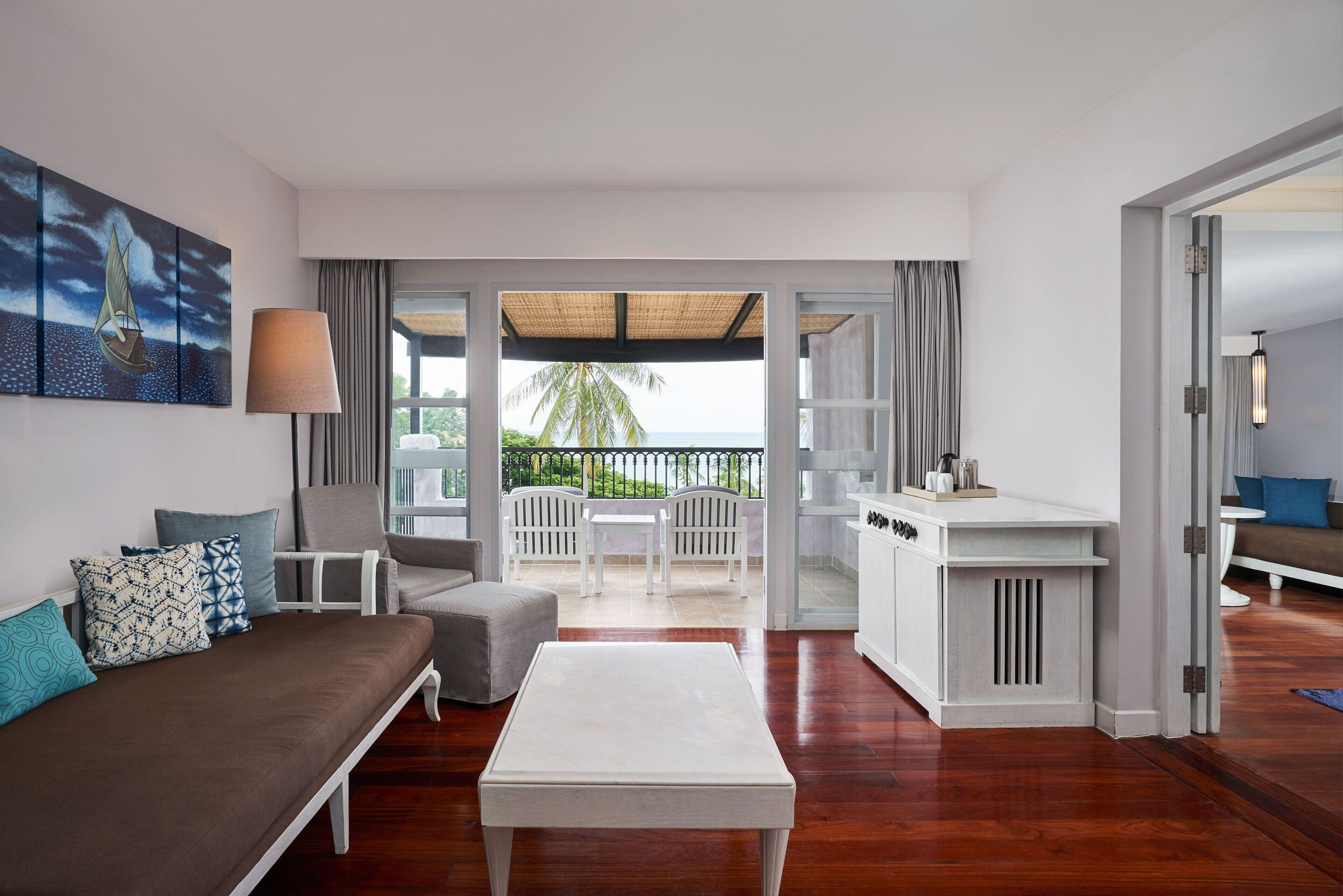 Una habitación de hotel moderna con suelo de madera, un sofá, una mesa, un balcón con vistas al mar y un cuadro en la pared.