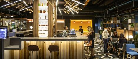 Zona de bar moderna con mostrador de madera, taburetes y suelo estampado.