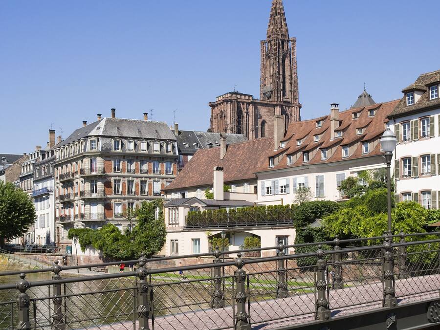 Un bâtiment historique surmonté d’une haute flèche, entouré d’une architecture européenne traditionnelle.