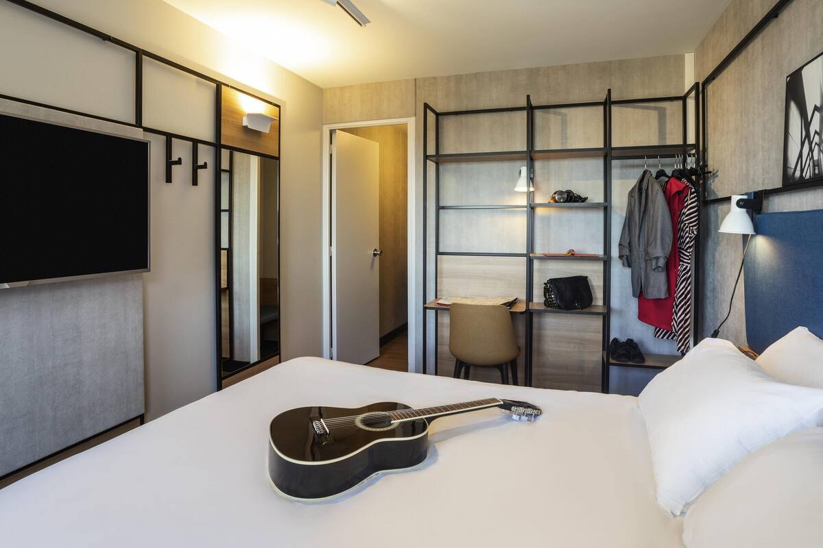 Een hotelkamer met een bed, een gitaar, een televisie, een kledingkast en een bureau.