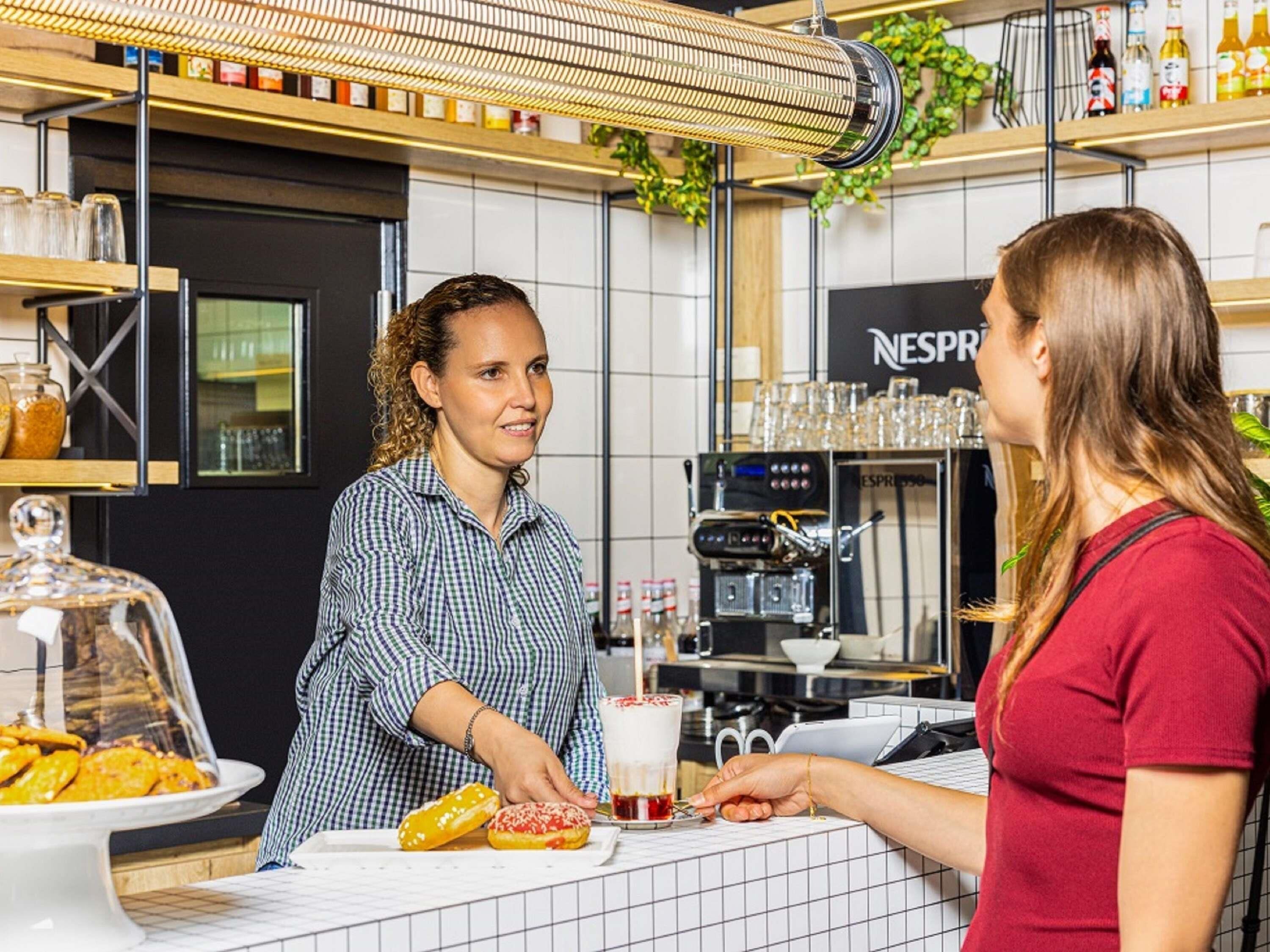 Un café doté d’une machine à café, d’un comptoir où sont exposées des pâtisseries et d’étagères remplies de condiments.
