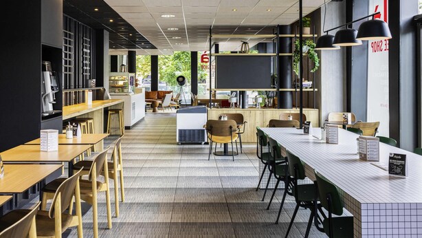 Ein modernes Café mit einer langen Theke, Sitzgelegenheiten und großen Fenstern.