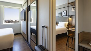 Ein Hotelzimmer mit Bett, Schreibtisch, Stuhl, Koffer und einem großen Fenster.