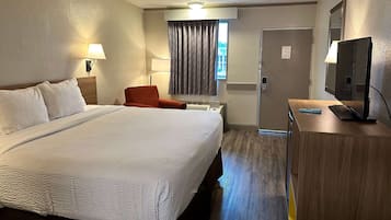 A hotel room with a large bed, a desk with a TV, a chair, a lamp, and a window with curtains.
