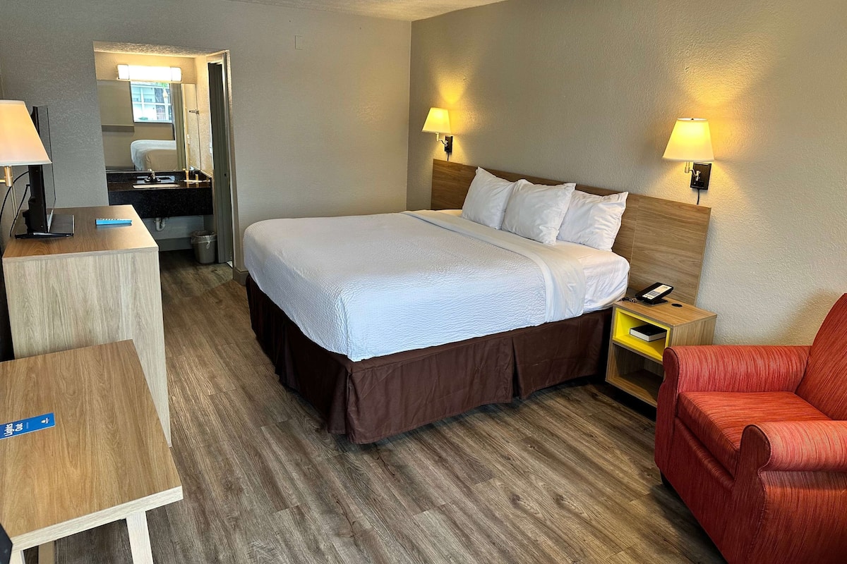 A hotel room with a bed, bedside lamps, a desk, a chair, and a small table.