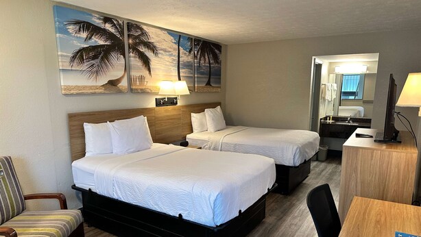 Habitación de hotel con dos camas, un escritorio, una silla, un espejo y obras de arte en la pared.