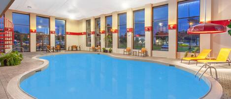 An indoor swimming pool with multiple seating areas and large windows.