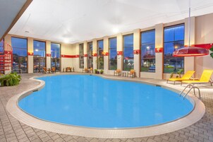 Una piscina interior con varias zonas de descanso y amplias ventanas.