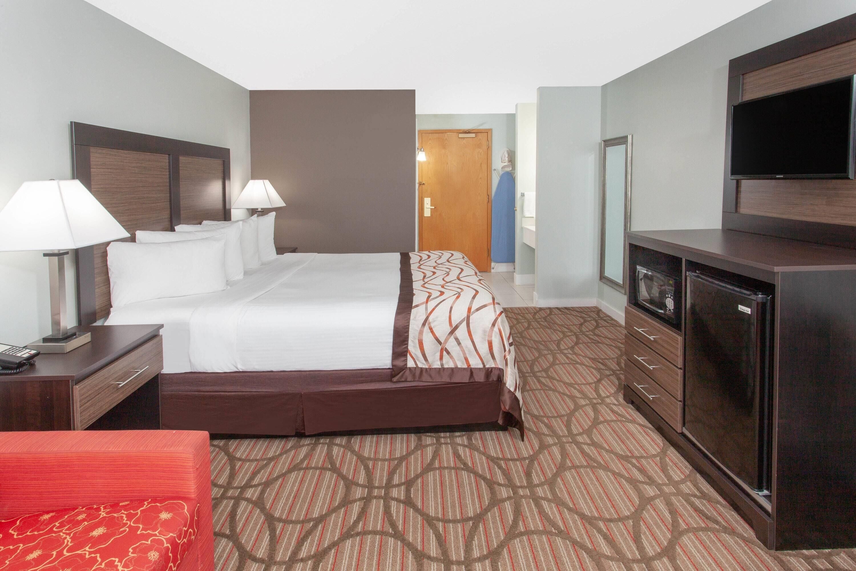 A hotel room with a bed, bedside lamps, a dresser, a TV, and a wardrobe.