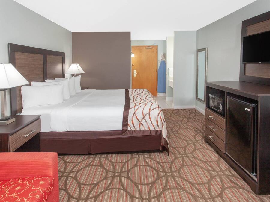A hotel room with a bed, bedside lamps, a dresser, a TV, and a wardrobe.
