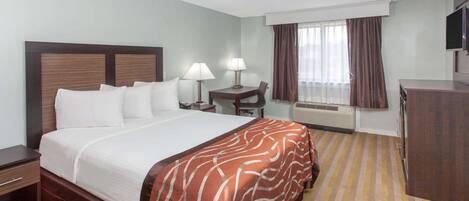 A hotel room with a large bed, a desk, a chair, a TV, and a window with curtains.