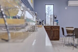 A modern kitchen with a long countertop, wooden cabinets, and a dining area with chairs. - Quality Inn & Suites Suffolk West (Suffolk)