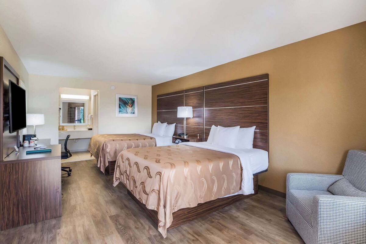 A hotel room with two beds, a desk, a TV, and a sofa.