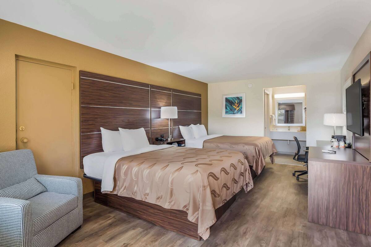 A hotel room with two beds, a desk, a chair, and a television.