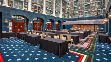 Un hall d’hôtel doté de nombreuses tables et chaises, d’un tapis à motifs et d’une vaste collection de tableaux encadrés accrochés aux murs.