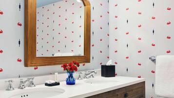 A bathroom with a vanity, two sinks, a mirror with lights, and a patterned wallpaper.