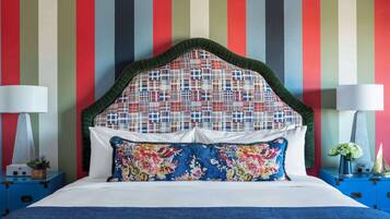 A bed with a colorful striped wall behind it, a floral pillow, and two bedside tables with lamps.