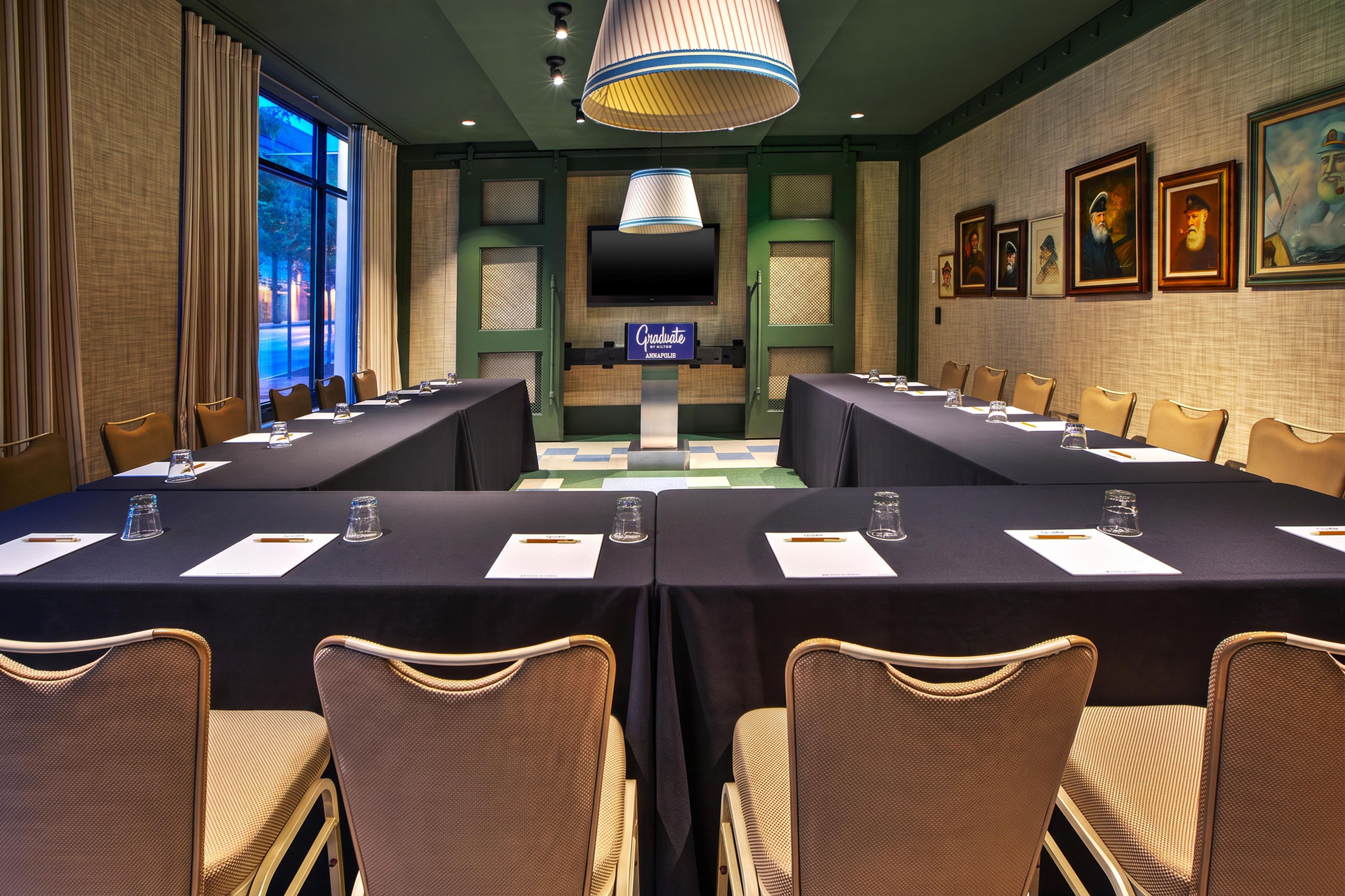 Une salle de conférence avec une longue table, des chaises, un écran de télévision et des tableaux encadrés accrochés au mur.