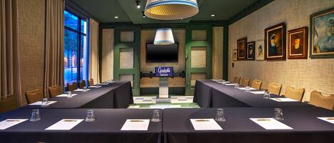 A conference room with a long table, chairs, a television screen, and framed pictures on the wall.