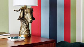 A lamp with a metallic animal head base, a white lampshade, and a striped wall in the background.