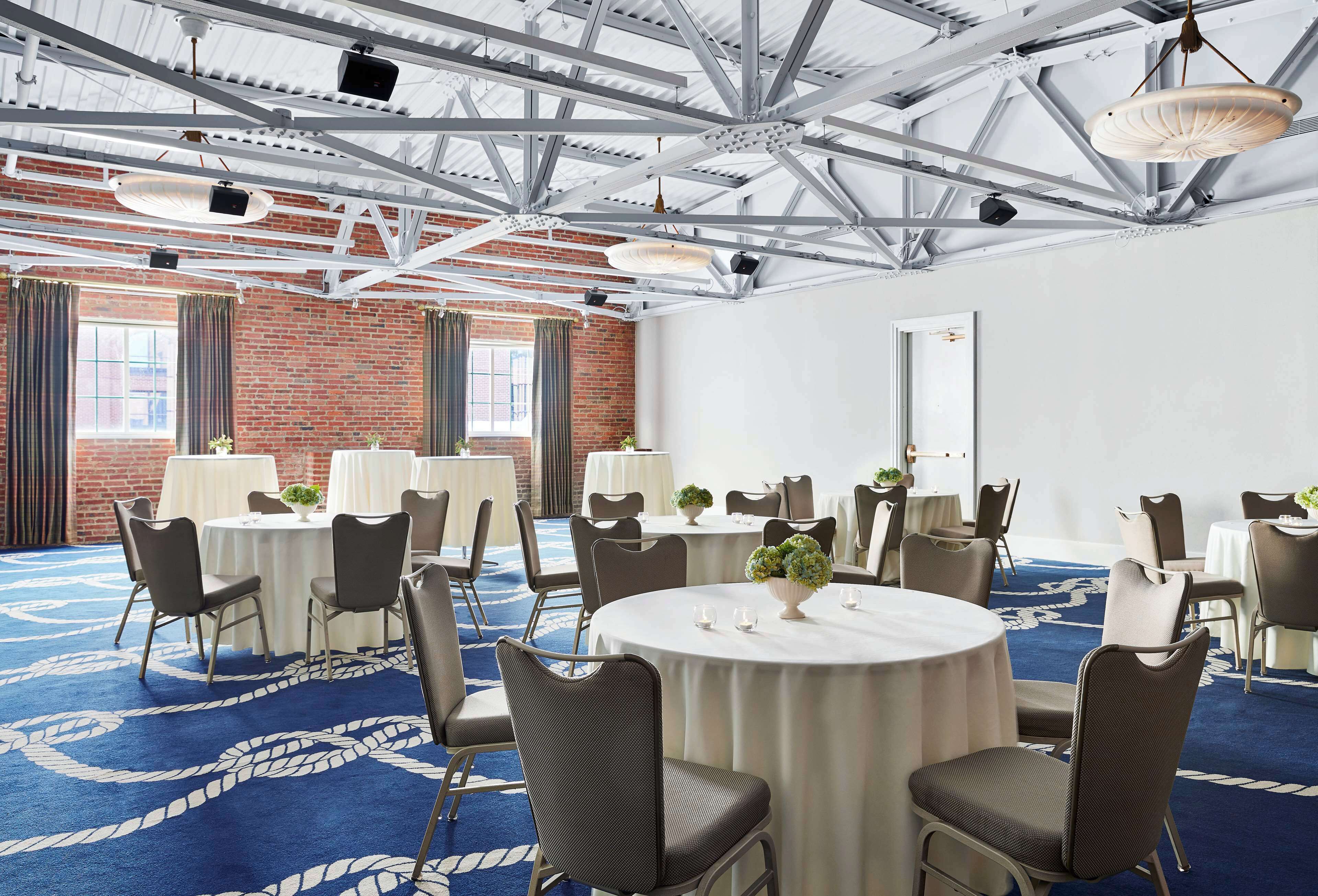 Un salón de conferencias con mesas redondas, sillas y una alfombra azul con diseño blanco.