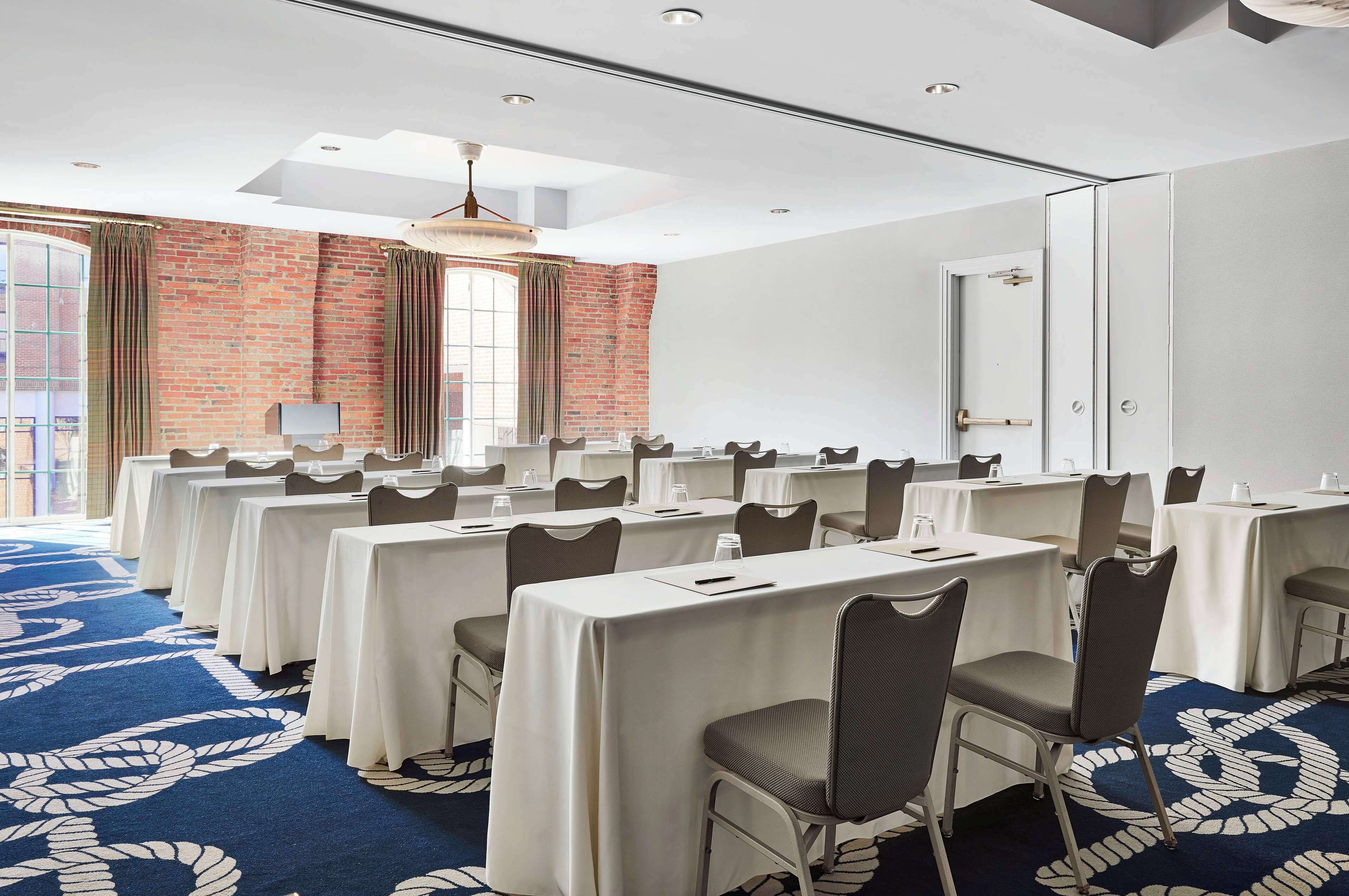 A conference room with multiple tables and chairs, a brick wall, and a large window.
