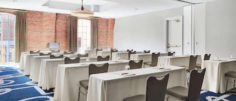Une salle de conférence dotée de plusieurs tables et de chaises, d’un mur en briques et d’une grande fenêtre.