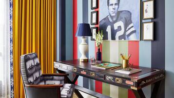 A room with a striped wall, a desk with a lamp, a chair, and framed artwork.