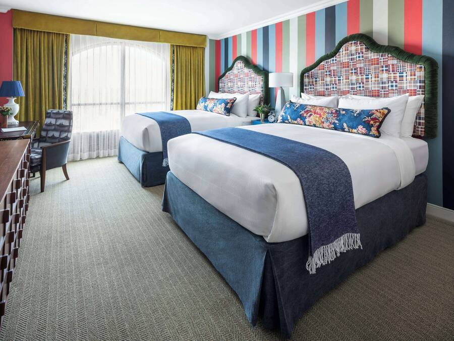 A hotel room with two beds, a desk, a chair, and a window with curtains.