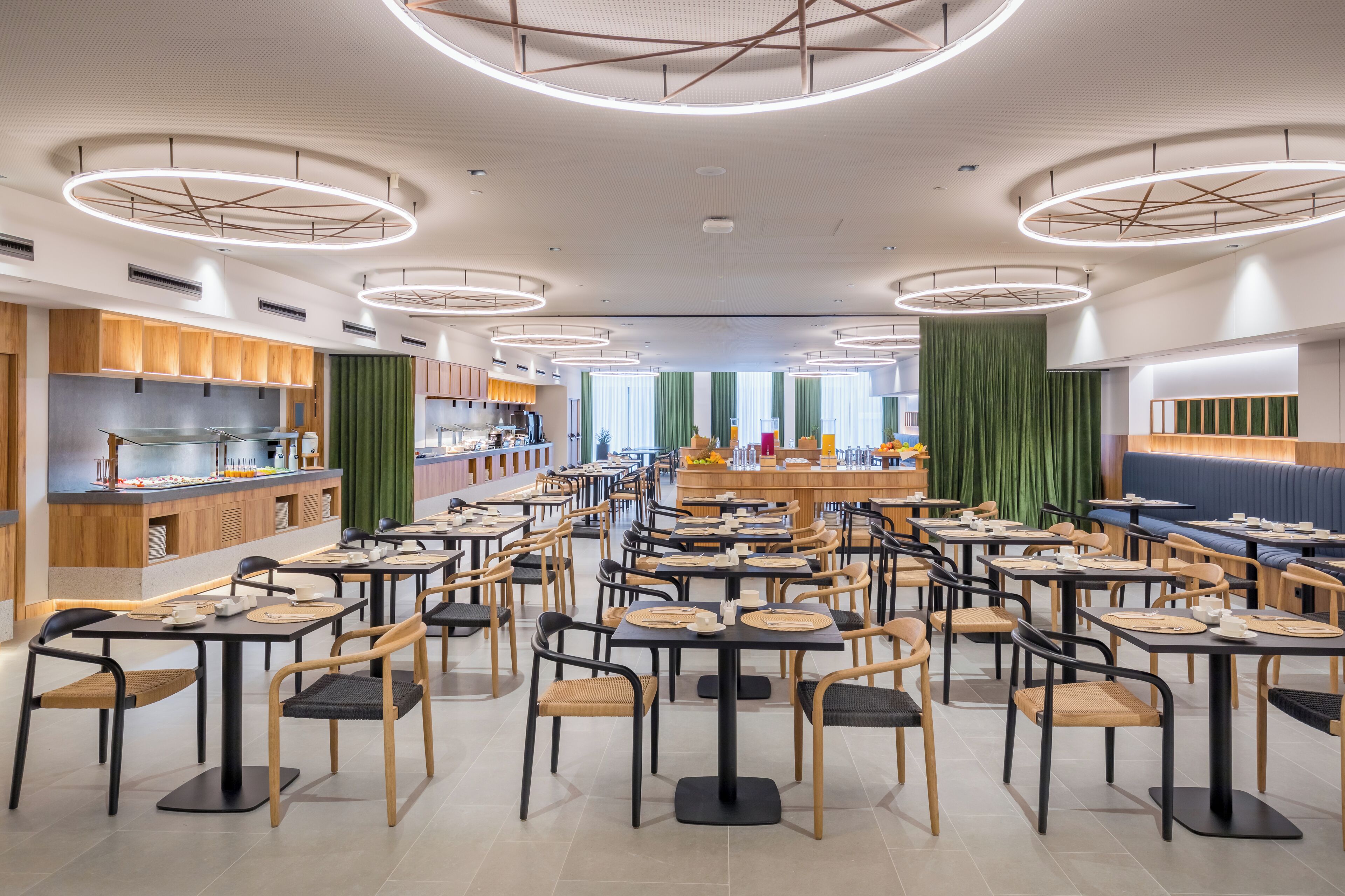 Un restaurant moderne avec des luminaires ronds au plafond, des meubles en bois et un espace de restauration central.
