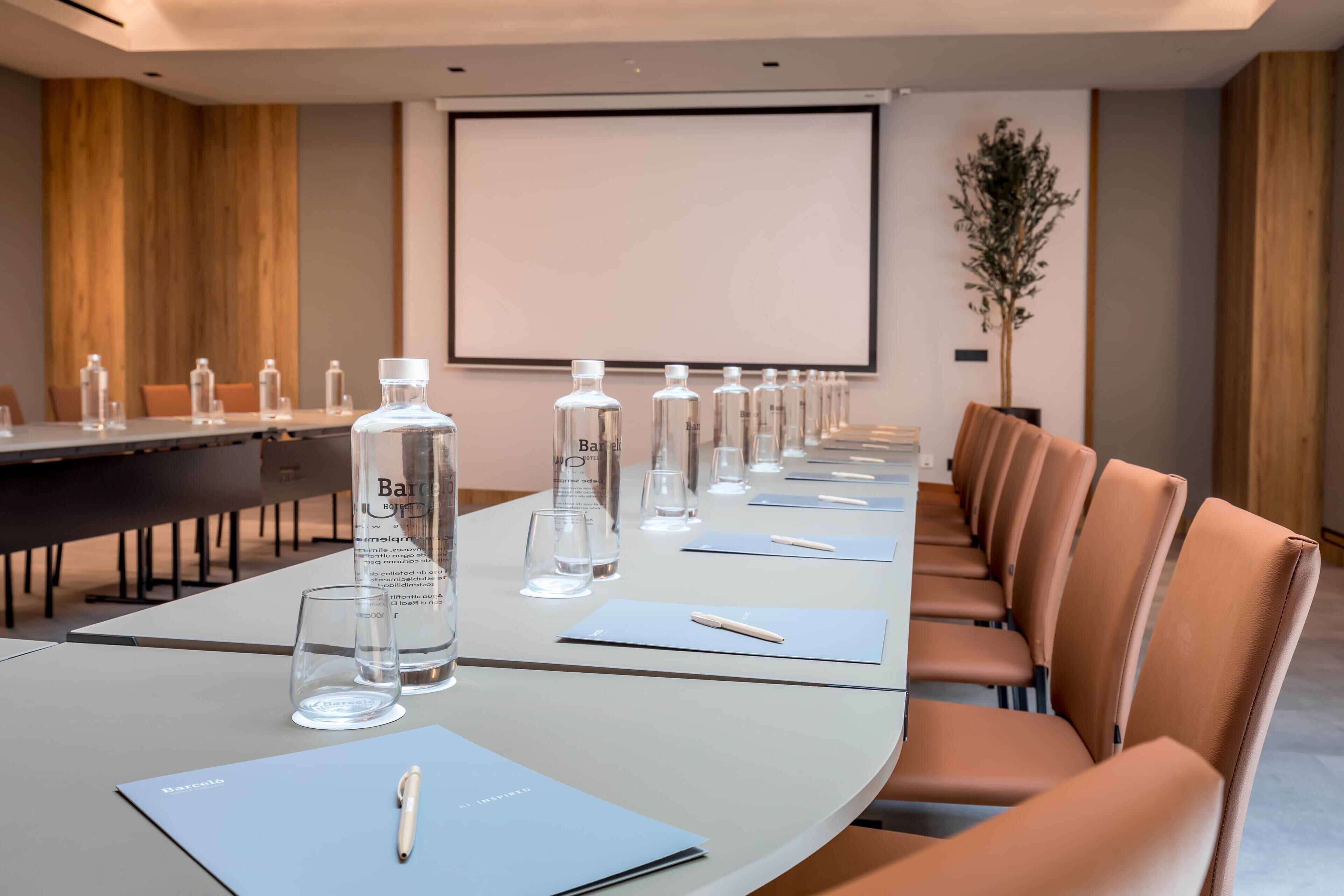 A conference room with a long table, chairs, water bottles, glasses, and a projector screen.